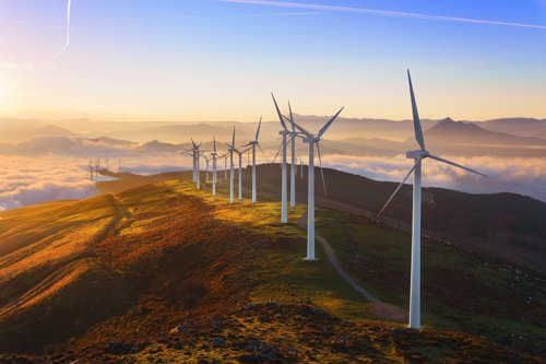 Kiwa inspected wind turbines on a hilltop at sunrise with a scenic view of mountains and clouds in the background