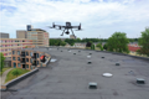 Drone hovering over a flat rooftop with surrounding buildings and trees, performing a drone inspection of the rooftop under a cloudy sky