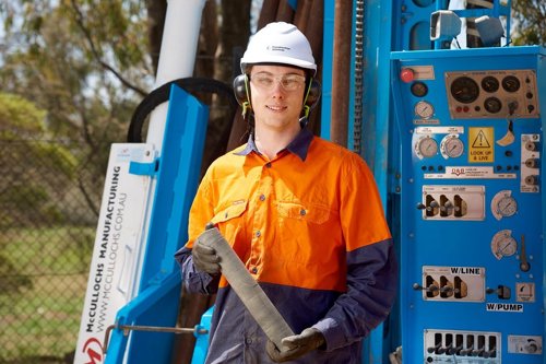Kiwa auditor in safety gear holding a core sample next to drilling equipment outdoors