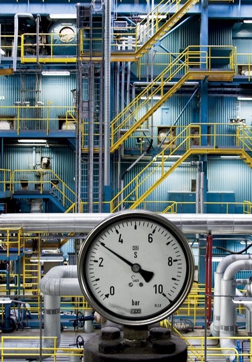 Industrial facility with pipes and a pressure gauge in the foreground.