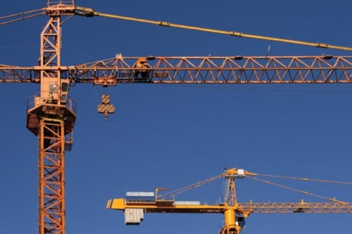 Two Kiwa inspected yellow construction cranes against a clear blue sky, showcasing industrial machinery used for building projects