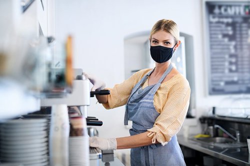 Vrouw in een schort maakt koffie bij een koffiemachine in een café met een menu op de achtergrond.