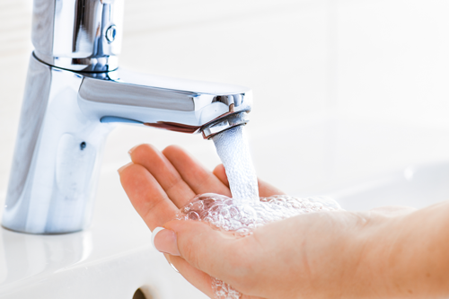 Hand under rinnande vatten från en kromad kran som är typgodkänd.