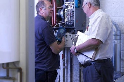 Two technicians inspecting and discussing a heating system in a utility room