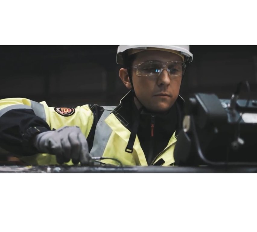Provningstekniker i varselkläder och skyddshjälm använder utför ultraljudsprovning i en industriell miljö.