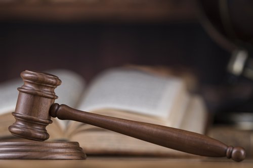 Houten hamer van een rechter op een houten onderstel, met een geopende wetboek en globes vaag op de achtergrond.