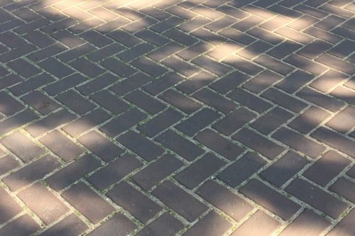 Grijs bakstenen straatpatroon in visgraatverband met zonlicht en schaduwen op het oppervlak.