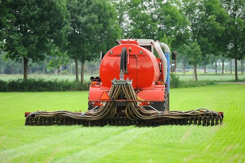 Rode mestinjecteurmachine met meerdere slangen op een groen grasveld