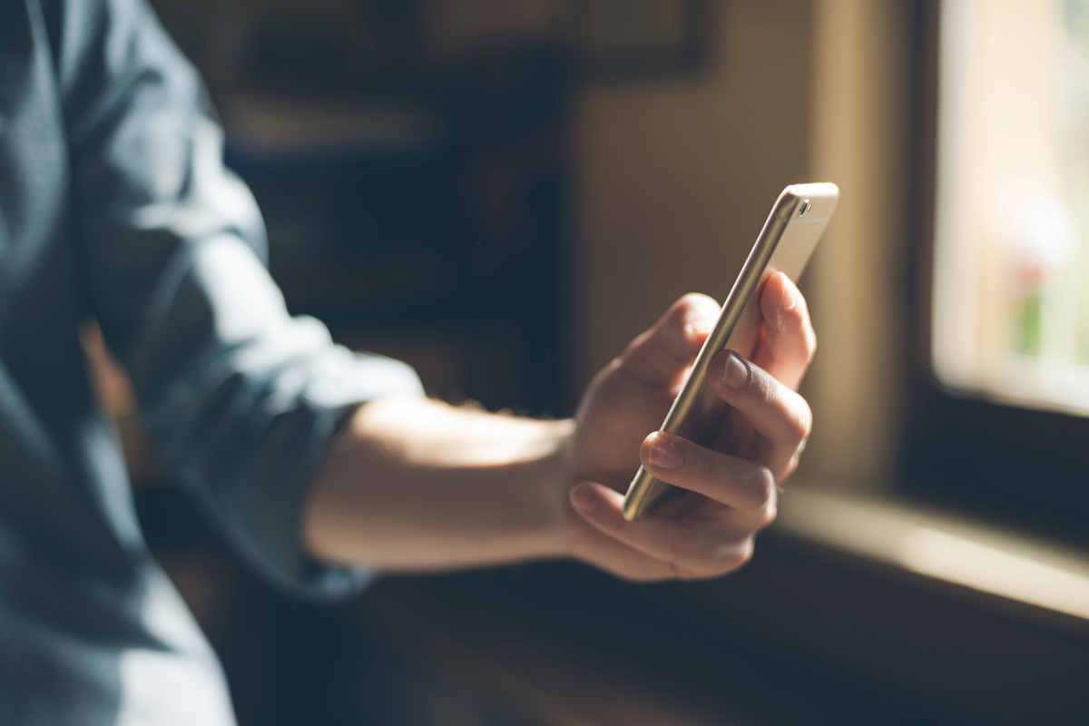 Een hand houdt een smartphone vast bij een raam met natuurlijk licht.
