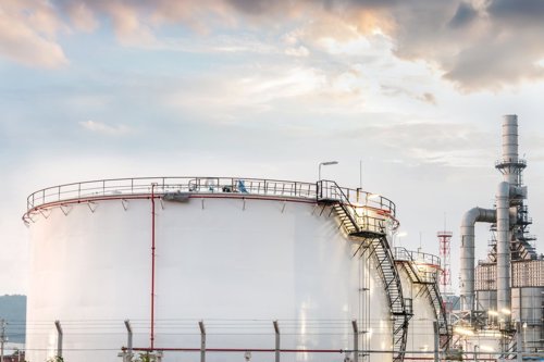 Opslagtanks voor olie of gas bij een industriële faciliteit, omringd door hekken en pijpleidingen onder een bewolkte hemel.