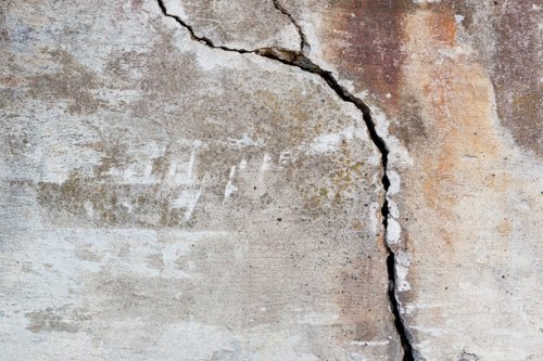 Betonnen oppervlak met een grote barst en verweerde plekken.