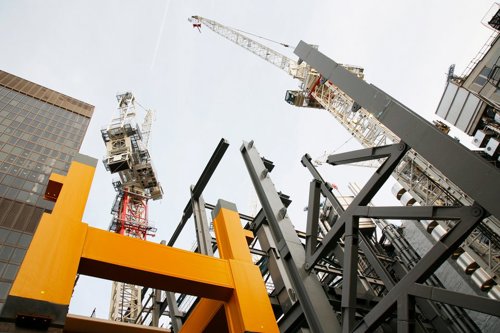 Flera byggkranar och stålkonstruktioner vid en byggarbetsplats, sedda från låg vinkel mot himlen - Kiwa håller i en kurs om stål, skador, svets och korrosion - en grundläggande kurs i materialteknik.