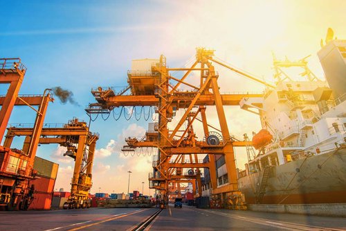 Containerhamn med stora orangea containerkranar, lastfartyg och soligt himmelssken - Kiwa anordnar seminariet Krandagarna 2026.