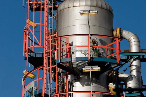 Industriell anläggning med stora silvertankar, röda metallräcken och rör mot blå himmel - gneom användning av databasen Matbas PED får du tillgång till information om vilka material som är godtagna under Tryckkärlsdirektivet PED.