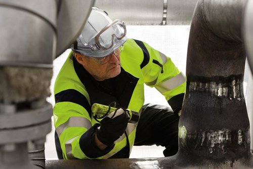 Arbetare i fluorescerande varselkläder inspekterar rörledningar i en industriell anläggning med tryckkärl eller lyftanordningar för att identifiera potentiella riskkällor och göra en noggrann riskbedömning.