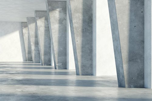 Betongväggar och pelare i en ljus, minimalistisk byggnad med solljus som skapar skuggor på golvet.