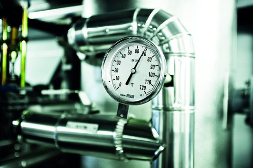 Manometer som mäter tryck, omgiven av metallrör i en industriell miljö.
