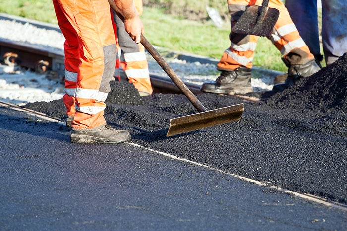 Workers laying asphalt on a road construction site, wearing orange safety gear and using shovels for paving
