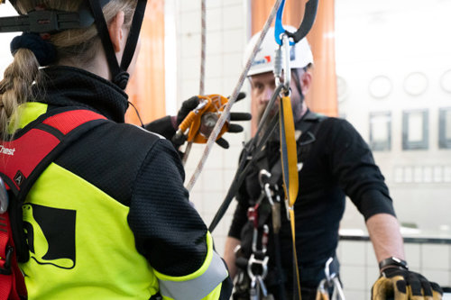 Personer utrustade med säkerhetssele och hjälm under en klättringsövning inomhus.