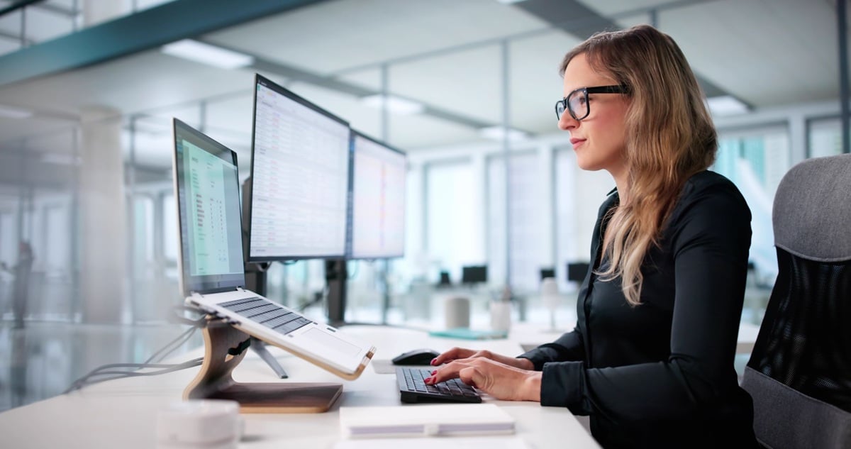 Woman working at a desk with multiple computer monitors in a modern office.