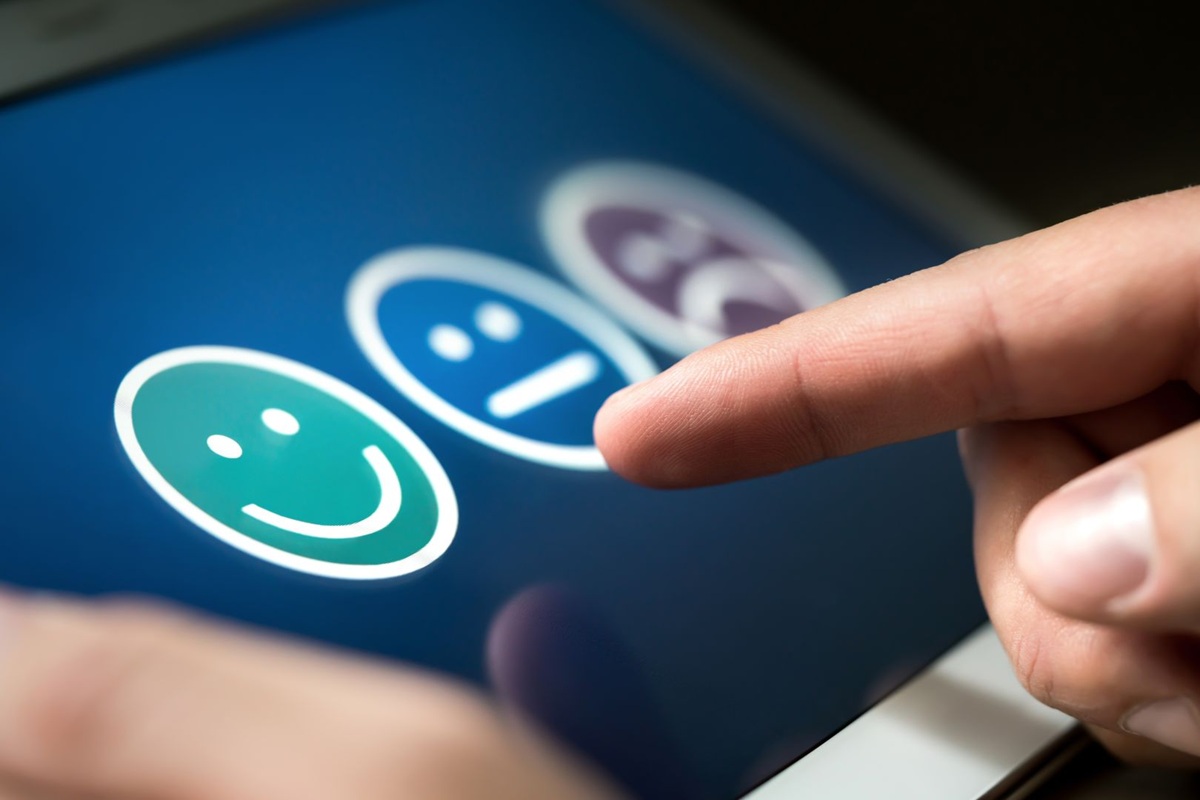 Vinger raakt een emoji op een touchscreen met drie gezichtsiconen in verschillende emoties.