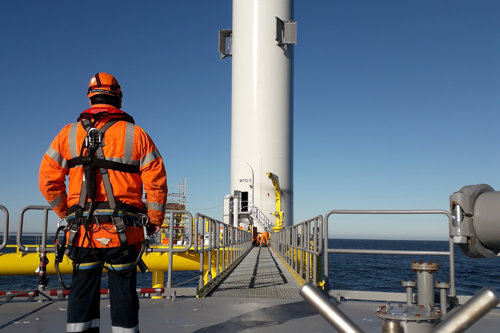 man standing in a platform of a standing windmill, to conduct a non-destructive test on the wind power asset