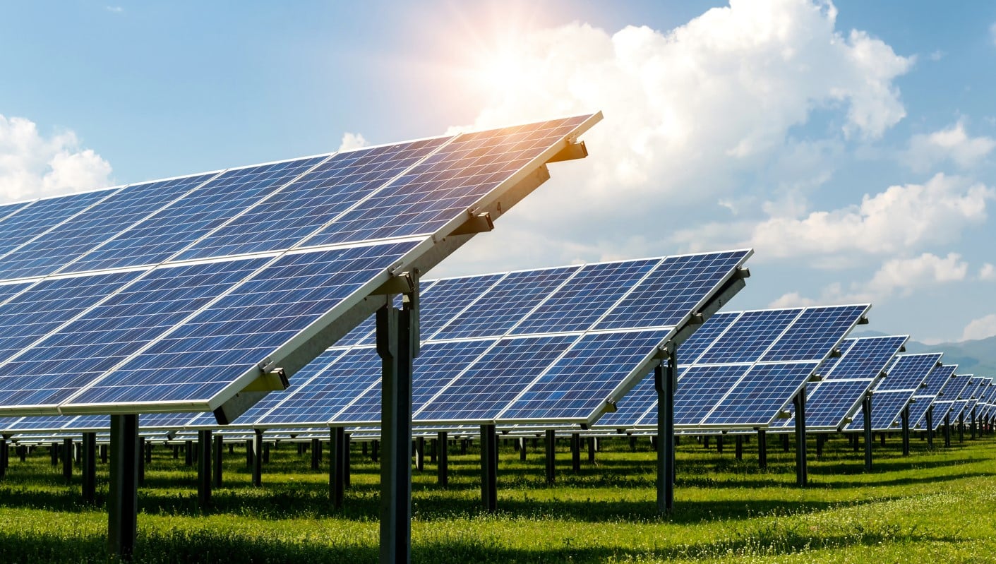 Solar panels installed in a green field under a sunny, partly cloudy sky.