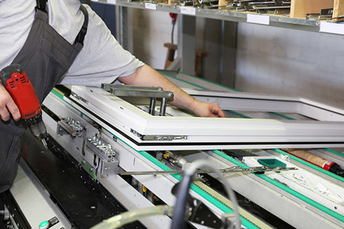 Person monterar ett fönster med en röd eldriven skruvdragare i en industriell verkstad - Kiwa erbjuder till dig som är tillverkare ett Byggproduktcertifikat - BPC.