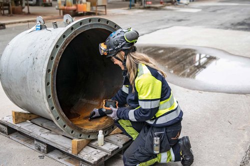 Inspektör i arbetskläder undersöker insidan av ett stort metallrör på en industriplats.