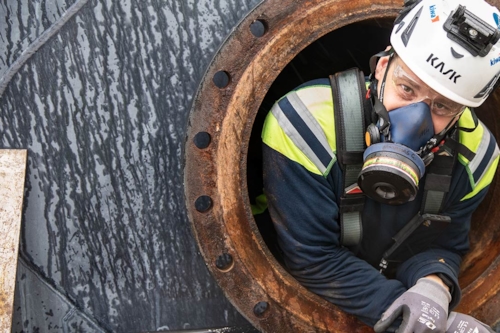 Man med gasmask tittar ut från arbete i slutet och trångt utrymme.
