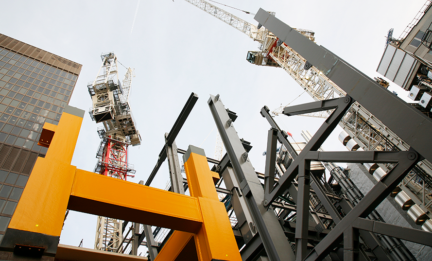 Industriell byggarbetsplats med höga kranar, betongbyggnader och stålkonstruktioner mot himlen.