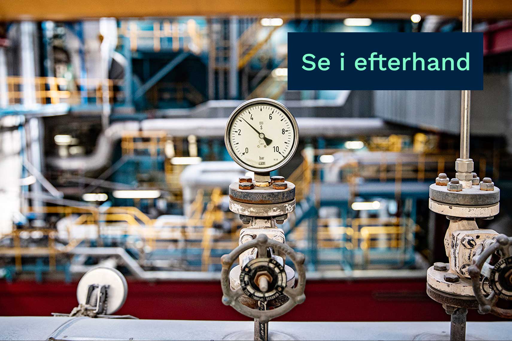 Tryckmätare och ventiler i en industriell anläggning med skylten ”Se i efterhand” i förgrunden.
