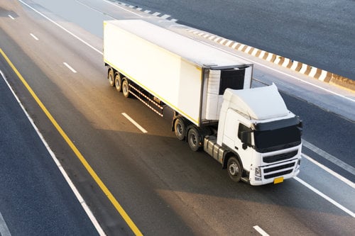 White semi-truck with a trailer driving on a multi-lane highway in daylight, illustrating transportation and logistics
