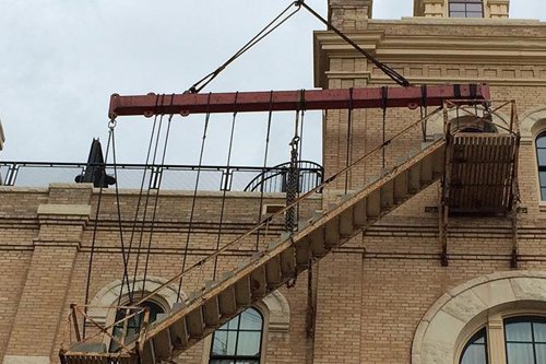 Old brick building facade with wooden outdoor staircase supported by a metal beam